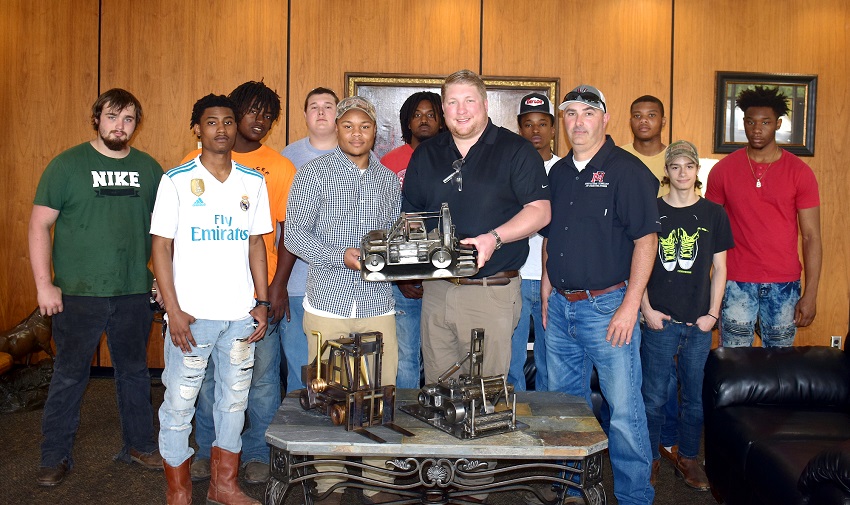 EMCC welding student Bryson Jenkins, at left center, and Davis Taylor pf Taylor Machine Works hold up a miniature sculpture of a Taylor Machine Works forklift made by Jenkins. EMCC and Jenkins are donating the sculpture that earned a first place in the Mississippi SkillsUSA Championships to Taylor Machine Works.