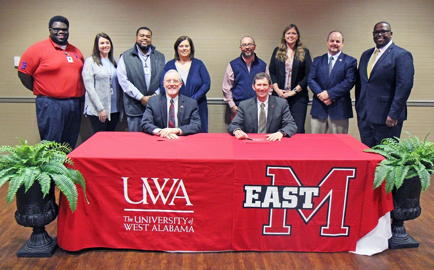 East Mississippi Community College President Dr. Scott Alsobrooks, seated at right, and University of West Alabama President Dr. Ken Tucker, seated at left, sign a memorandum of understanding that guarantees admission to UWA for all EMCC students with a grade point average of a 2.0 or higher. EMCC Executive Director of College Advancement & Athletics Marcus Wood, back row, second from right, was among those in attendance. Others pictured are EMCC employees who graduated from UWA. They are, back row, from left: math instructor Jonathan Woodruff; biology instructor Ashley Richardson; biology instructor Jairus Johnson; English instructor Janet Briggs; English instructor Derrick Conner; Communiversity Executive Director Dr. Courtney Taylor; and Associate Dean of Instruction and Interim Vice President of Instruction James Rush.