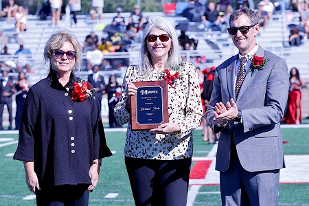 East Mississippi Community College’s 2025 Alumnus of the Year, Richard Poole, was unable to attend the college’s Homecoming. Poole’s award was accepted by his niece, Melinda Brown, at center, during halftime of EMCC’s annual Homecoming game. The award was presented by Director of Alumni Affairs and Foundation Operations Gina Cotton, left, and EMCC President Dr. Scott Alsobrooks, at right. 